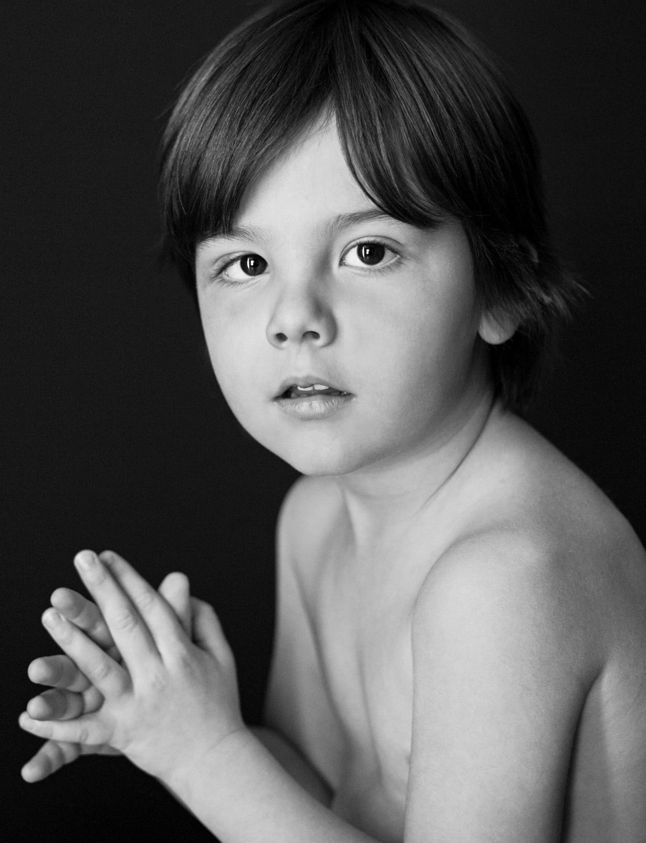 studio portrait on black of a young shirtless boy in shorts